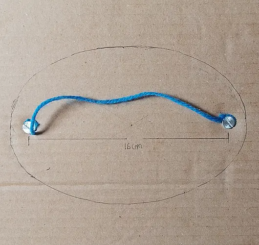 Trazo de una elipse dibujada en cartón utilizando el método del jardinero con dos tornillos como focos y un hilo azul de fijación