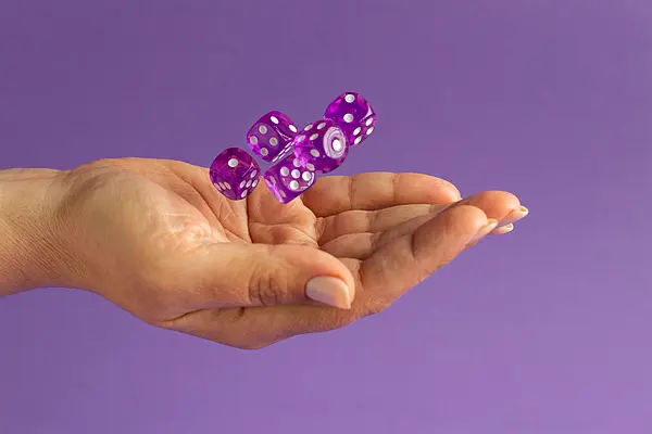 Fotografía de una mano abierta arrojando al aire varios dados de color morado translúcido sobre un fondo liso morado, empleada para representar un experimento aleatorio es un ejemplo del tema experimentos aleatorios y deterministas